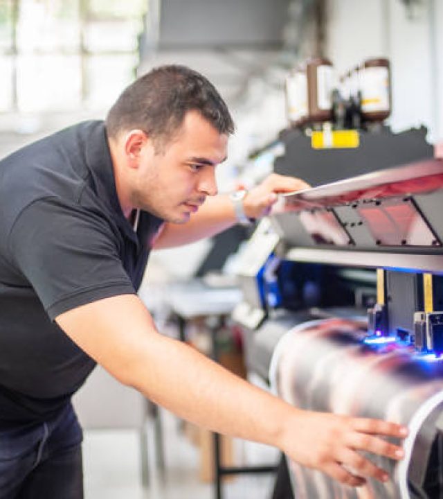 In the printing house, an experienced technician works on a UV printer. Production work. Check the print quality.